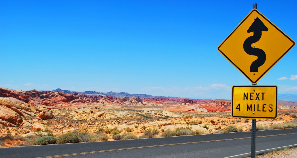 Lonely desert road with a sign showing curves ahead.