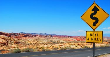 Lonely desert road with a sign showing curves ahead.