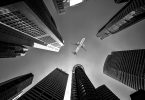 Black and white image looking between skyscrapers at an airplane overhead.
