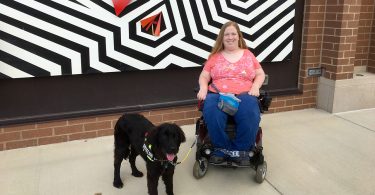 Karin Willison with my service dog sitting in my wheelchair outside in front of a zigzag mural.